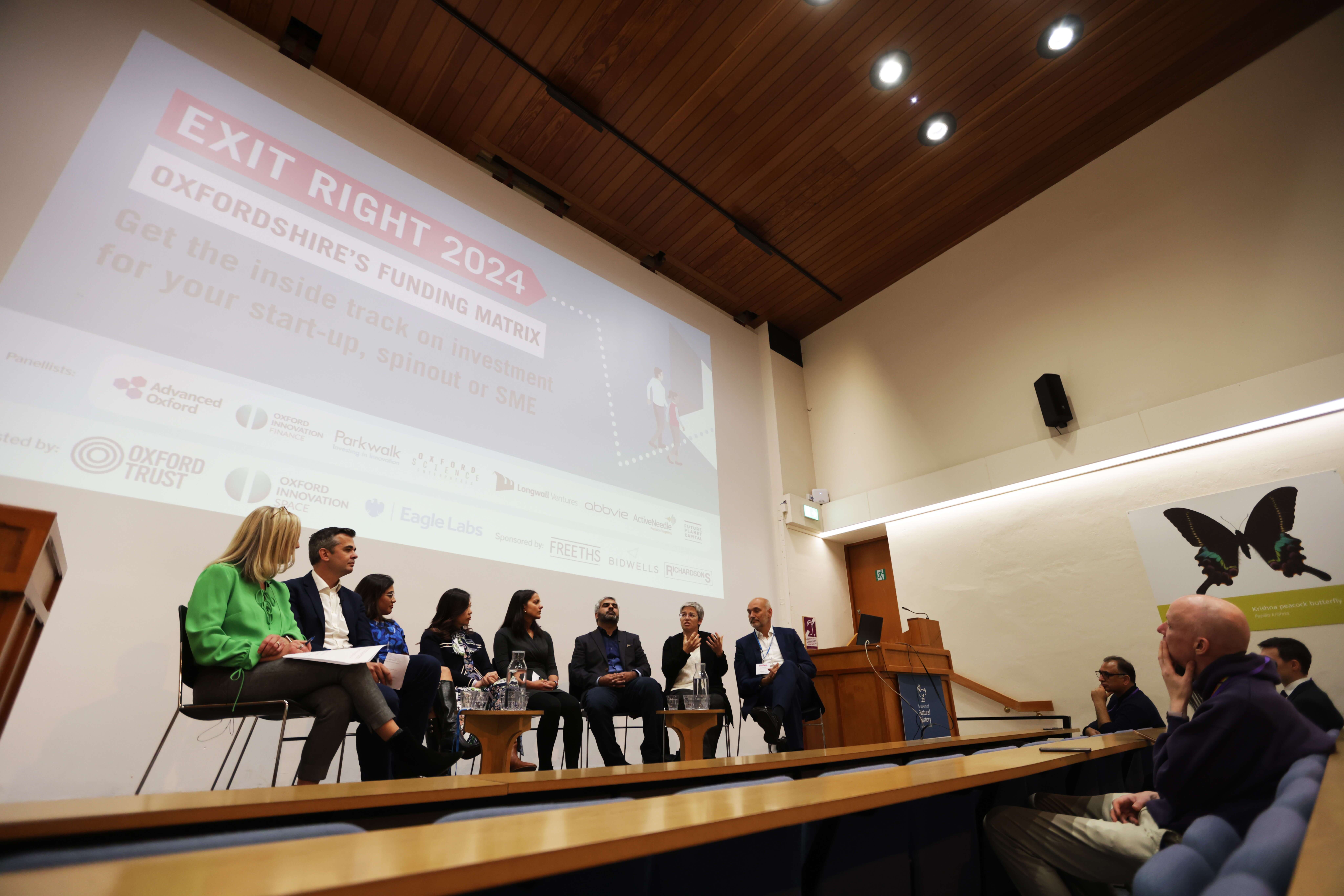 Panellists at the Exit Right event sit on a stage with a large screen behind facing the audience.