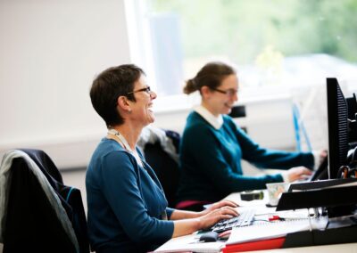 Two colleagues sit at a desk with a window behind at the Wood Centre for Innovation.