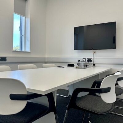A six person meeting room at the Wood Centre for Innovation showing a table, six white chairs, a screen and water glasses.